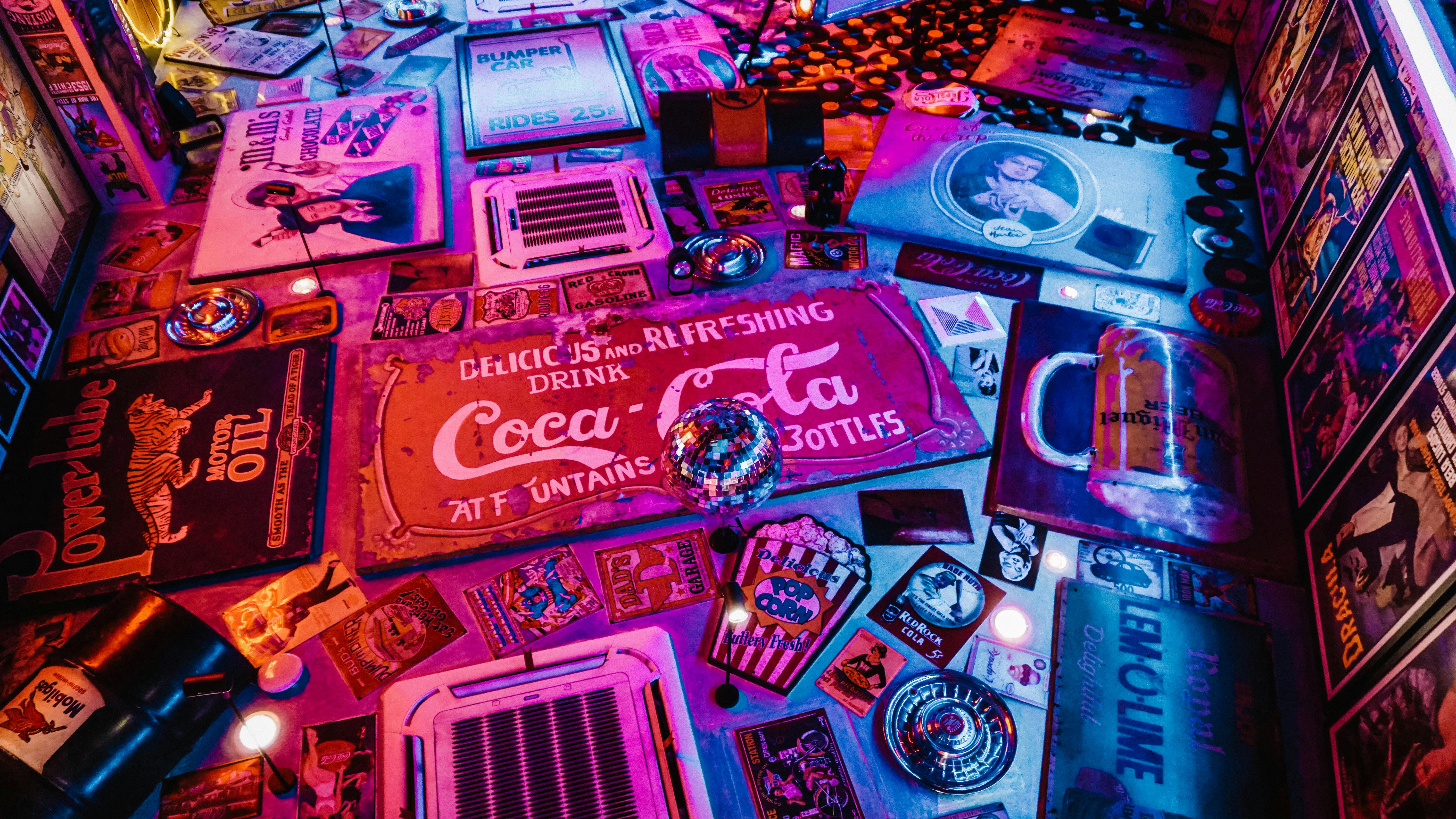Retro-themed neon collage with vintage Coca-Cola signs, classic movie posters, vinyl records, and nostalgic automotive memorabilia.